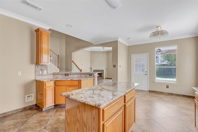 kitchen with ceiling fan with notable chandelier, light stone countertops, a center island, and crown molding