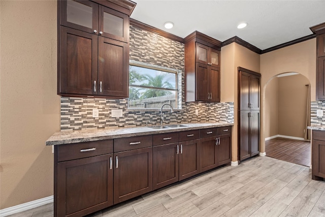 kitchen with decorative backsplash, light stone countertops, sink, and crown molding