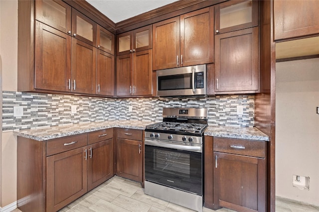 kitchen with appliances with stainless steel finishes, light stone counters, and tasteful backsplash