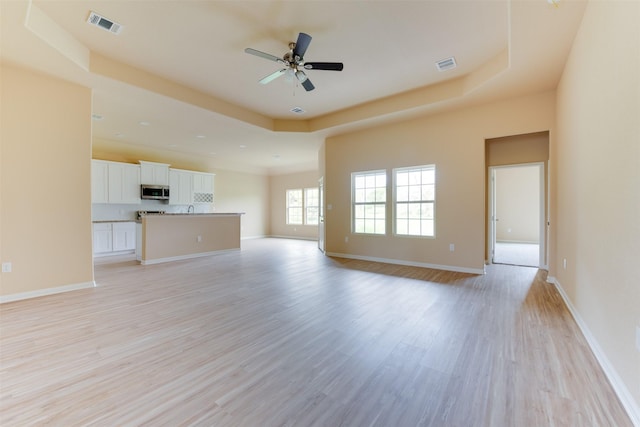 unfurnished living room featuring ceiling fan, light wood-type flooring, and a tray ceiling