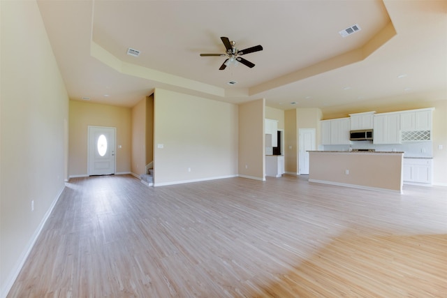 unfurnished living room with ceiling fan, a tray ceiling, and light hardwood / wood-style flooring