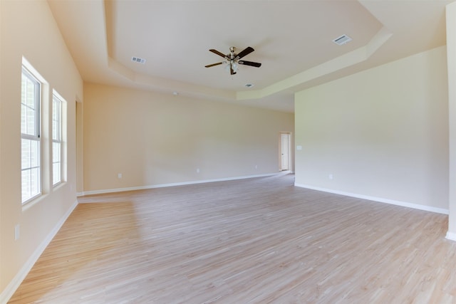 unfurnished room with a wealth of natural light, a tray ceiling, and light hardwood / wood-style flooring