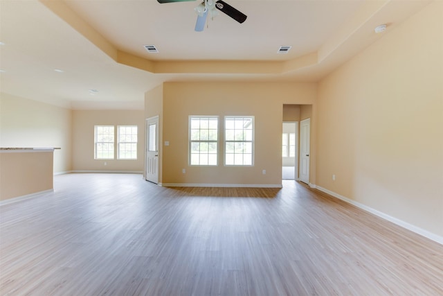 spare room with a raised ceiling, light wood-type flooring, and ceiling fan