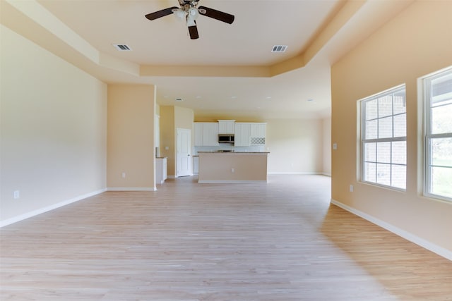 unfurnished living room with ceiling fan, a raised ceiling, and light hardwood / wood-style flooring