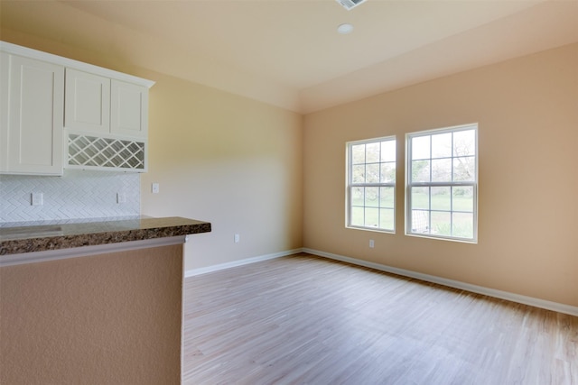 kitchen featuring light wood-type flooring, white cabinets, decorative backsplash, and dark stone countertops