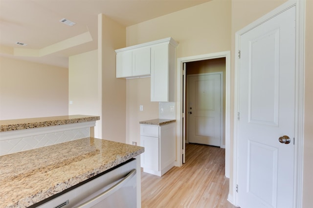 kitchen with a tray ceiling, light wood-type flooring, light stone countertops, stainless steel dishwasher, and white cabinets