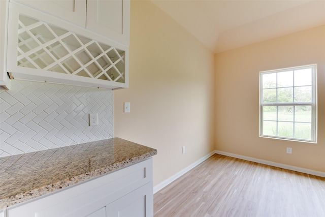 kitchen featuring light wood-type flooring, backsplash, light stone counters, and white cabinetry