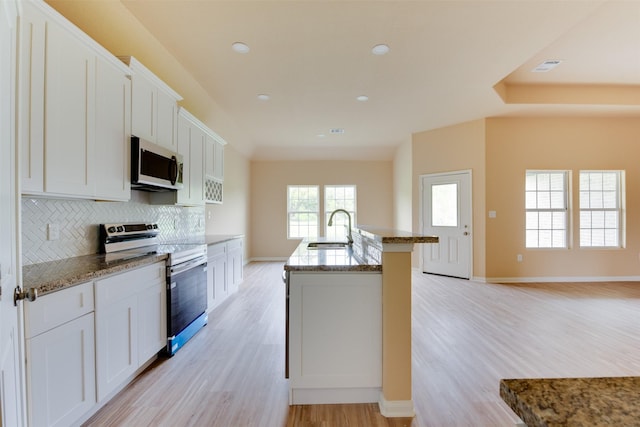 kitchen featuring white cabinetry, stainless steel appliances, decorative backsplash, a kitchen island with sink, and sink