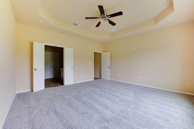 unfurnished bedroom featuring ceiling fan, a raised ceiling, and carpet floors