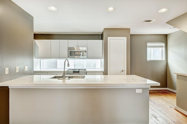 kitchen with stainless steel appliances, white cabinets, light stone countertops, light hardwood / wood-style flooring, and sink