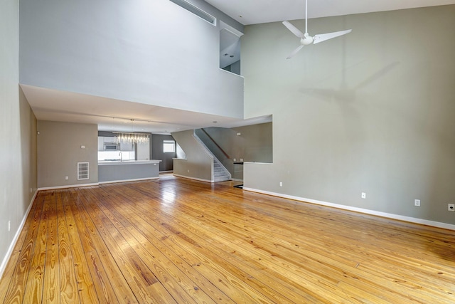 unfurnished living room with high vaulted ceiling, ceiling fan with notable chandelier, and light hardwood / wood-style floors