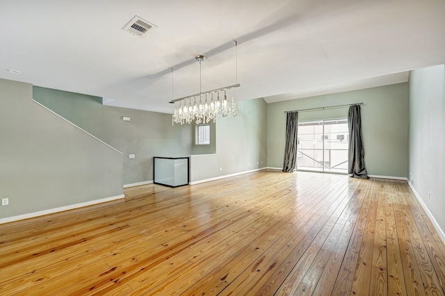 unfurnished living room with light wood-type flooring, a chandelier, and a healthy amount of sunlight