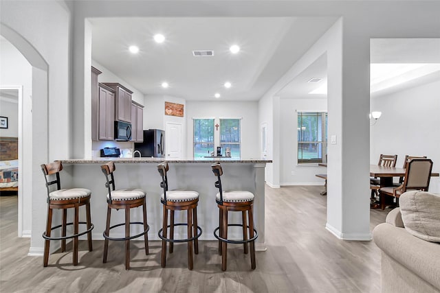 kitchen with stainless steel fridge with ice dispenser, a breakfast bar area, light hardwood / wood-style floors, and kitchen peninsula