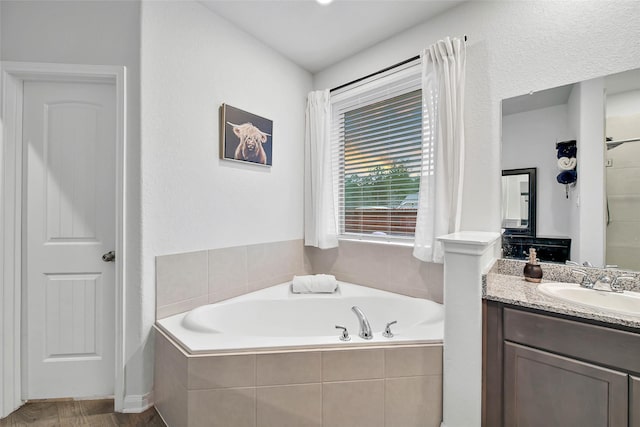 bathroom featuring hardwood / wood-style flooring, tiled tub, and vanity