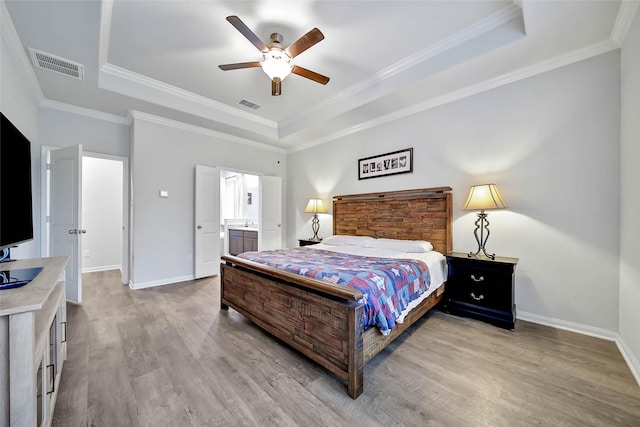 bedroom with ceiling fan, ensuite bathroom, a raised ceiling, crown molding, and light hardwood / wood-style flooring