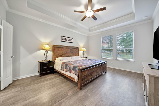 bedroom with ceiling fan, crown molding, wood-type flooring, and a raised ceiling