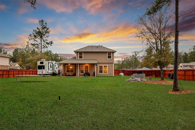 back house at dusk featuring a trampoline, a patio area, and a yard