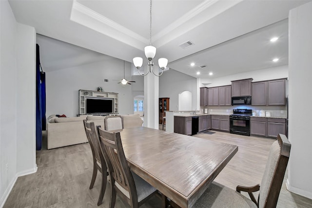 dining room with ceiling fan with notable chandelier, a tray ceiling, ornamental molding, and light wood-type flooring