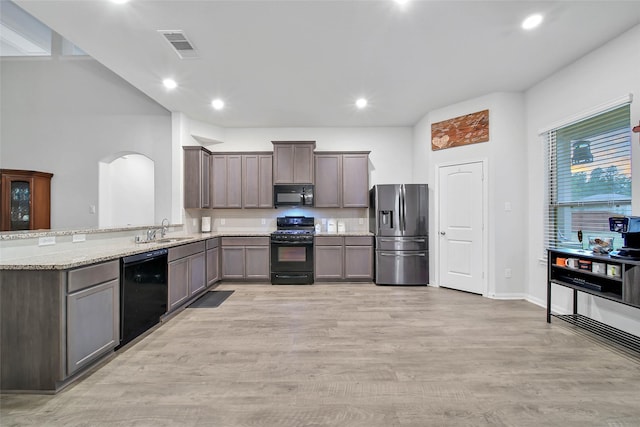 kitchen featuring light stone countertops, black appliances, sink, kitchen peninsula, and light hardwood / wood-style flooring