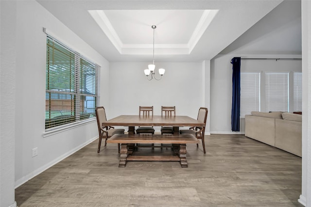 dining space with hardwood / wood-style floors, a raised ceiling, and an inviting chandelier