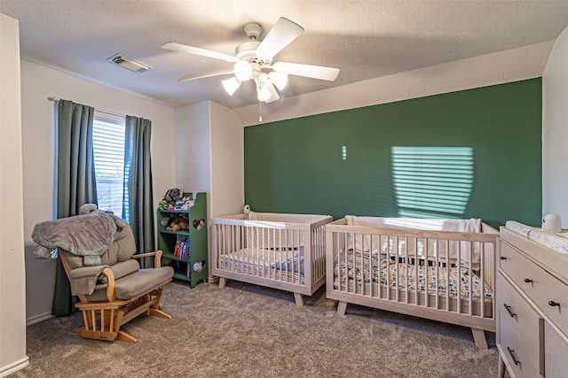 bedroom with ceiling fan, a textured ceiling, a crib, and carpet floors