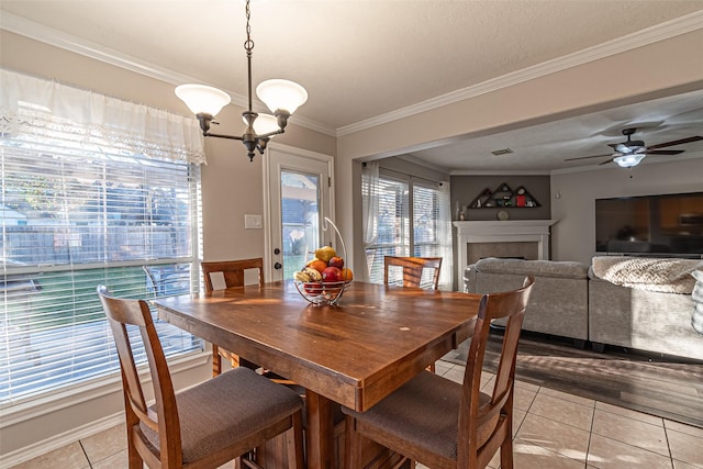 tiled dining room with ceiling fan with notable chandelier, ornamental molding, and a tiled fireplace