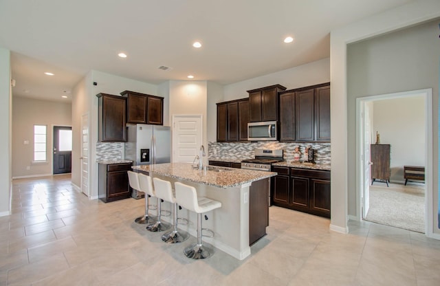 kitchen featuring stainless steel appliances, an island with sink, sink, a kitchen breakfast bar, and light stone counters