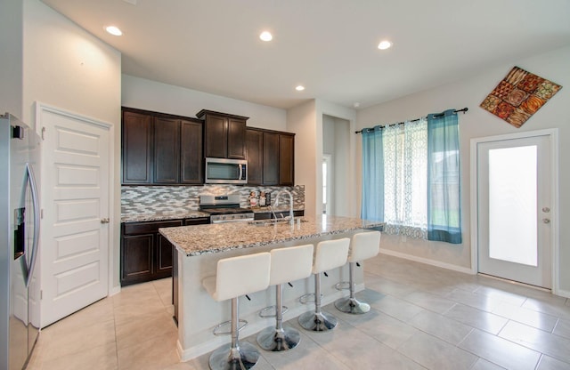 kitchen with sink, a kitchen island with sink, a breakfast bar area, stainless steel appliances, and light tile patterned floors