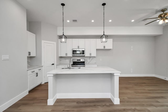 kitchen featuring light stone countertops, a kitchen island with sink, appliances with stainless steel finishes, and white cabinetry