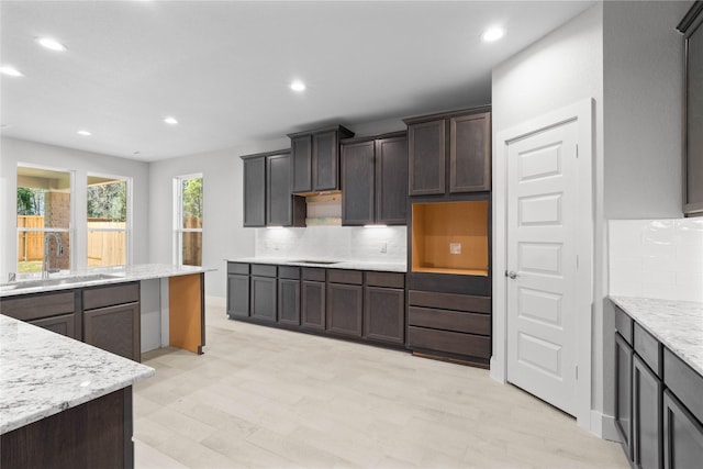 kitchen featuring decorative backsplash, sink, light hardwood / wood-style flooring, dark brown cabinetry, and light stone countertops