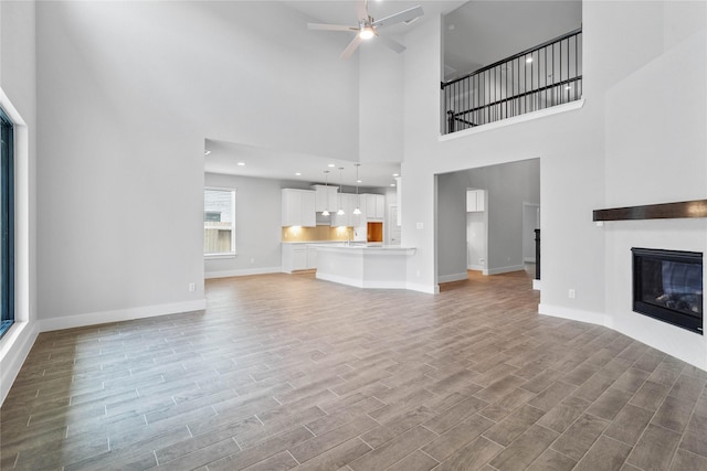 unfurnished living room featuring wood finished floors, baseboards, a ceiling fan, and a glass covered fireplace
