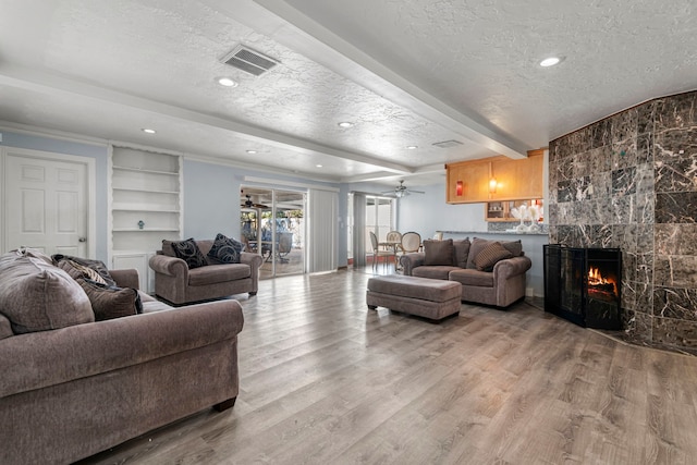 living room with a textured ceiling, ceiling fan, a large fireplace, and beamed ceiling