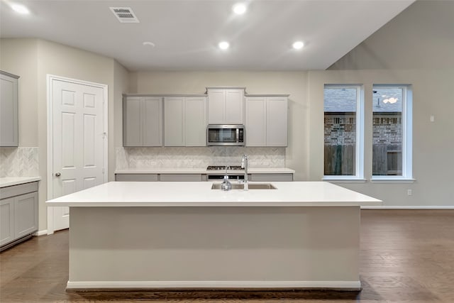 kitchen with sink, gray cabinetry, a kitchen island with sink, and tasteful backsplash