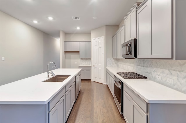 kitchen featuring a center island with sink, decorative backsplash, sink, gray cabinetry, and stainless steel appliances