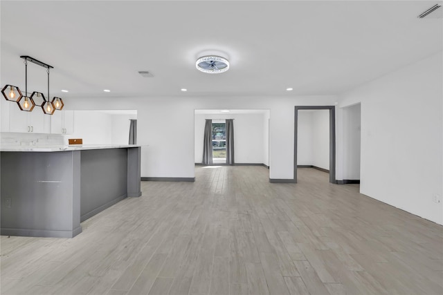 interior space featuring tasteful backsplash, white cabinets, light hardwood / wood-style floors, and decorative light fixtures