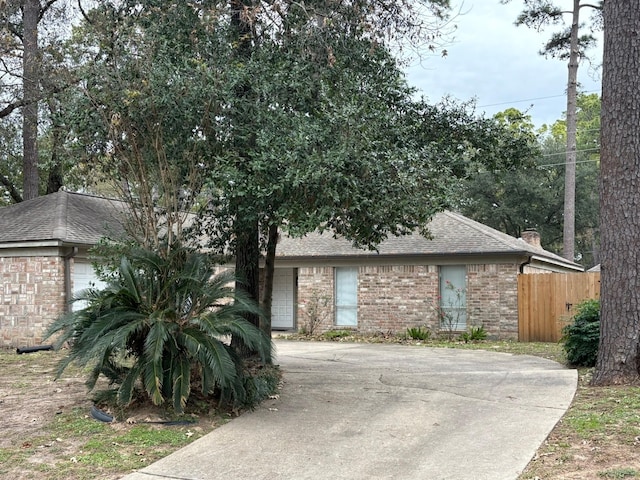 view of front facade with a shingled roof, a chimney, an attached garage, fence, and brick siding