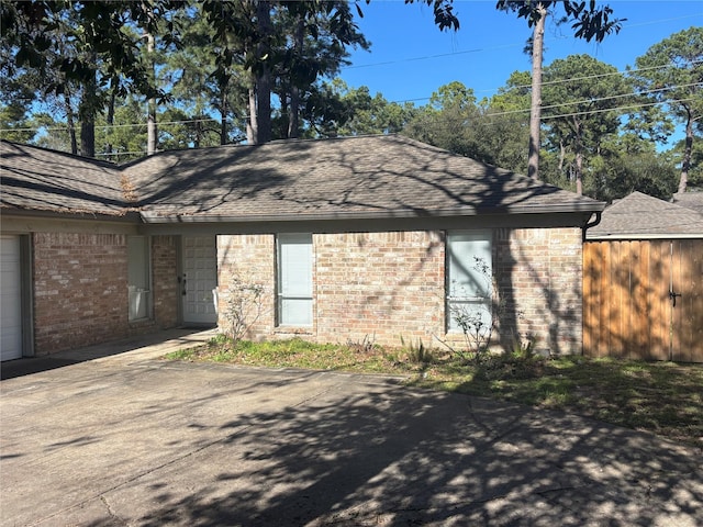 back of property featuring roof with shingles, brick siding, an attached garage, and fence