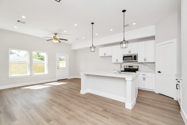 kitchen featuring pendant lighting, white cabinets, stainless steel appliances, a kitchen island with sink, and ceiling fan