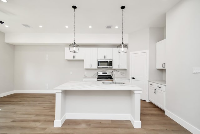 kitchen with decorative light fixtures, a center island with sink, electric range, and light stone countertops