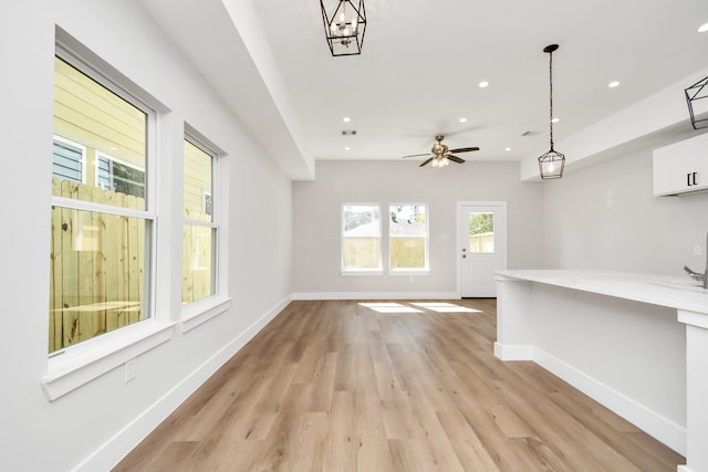 unfurnished living room with ceiling fan with notable chandelier and light hardwood / wood-style flooring