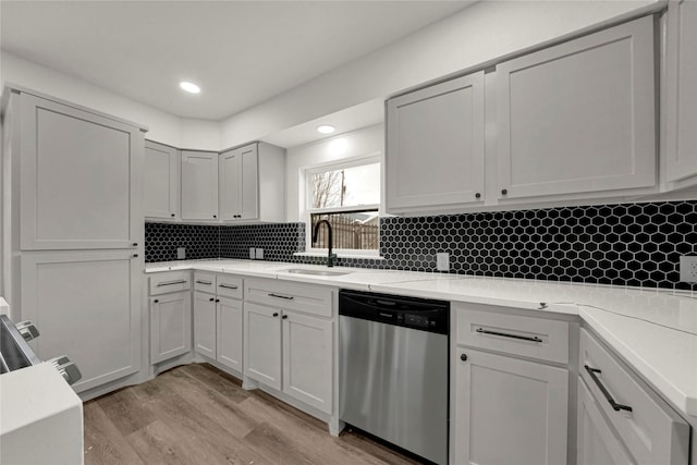 kitchen with light wood-type flooring, decorative backsplash, stainless steel dishwasher, and sink