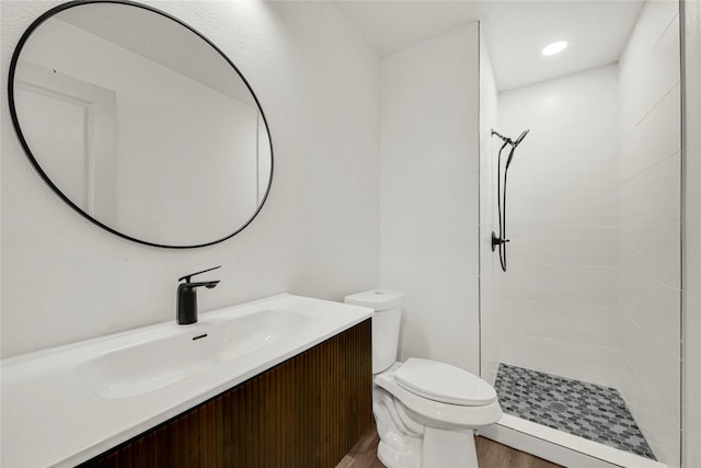 bathroom featuring wood-type flooring, toilet, vanity, and tiled shower