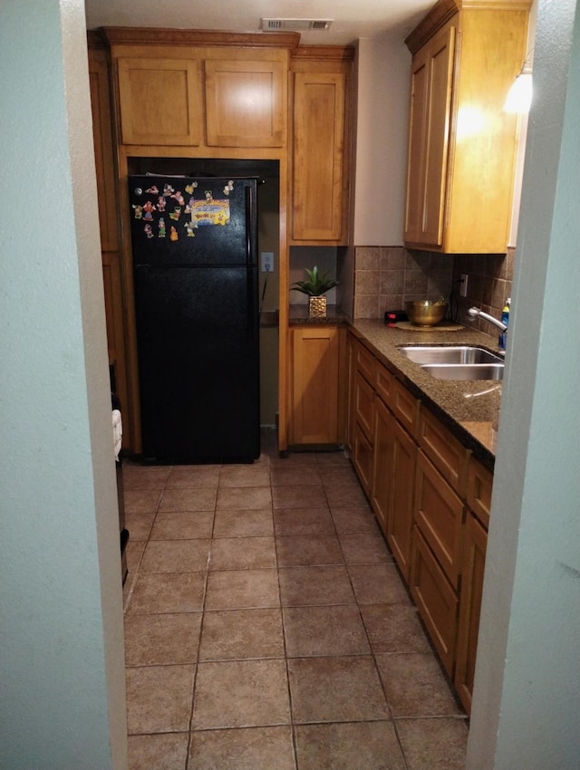 kitchen featuring black refrigerator, backsplash, sink, and dark stone counters