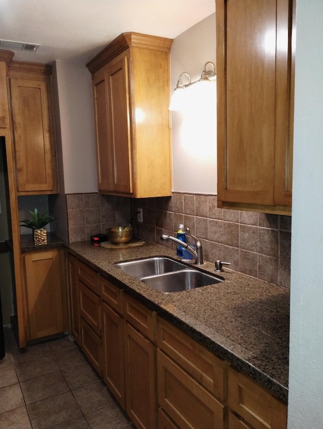 kitchen featuring sink, dark tile patterned flooring, dark stone countertops, and tasteful backsplash