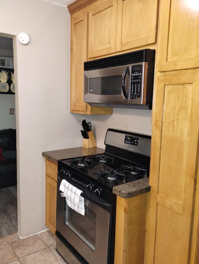 kitchen with light tile patterned flooring, appliances with stainless steel finishes, and dark stone countertops