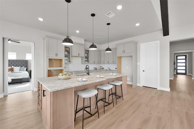 kitchen with sink, hanging light fixtures, a large island, light stone countertops, and light wood-type flooring