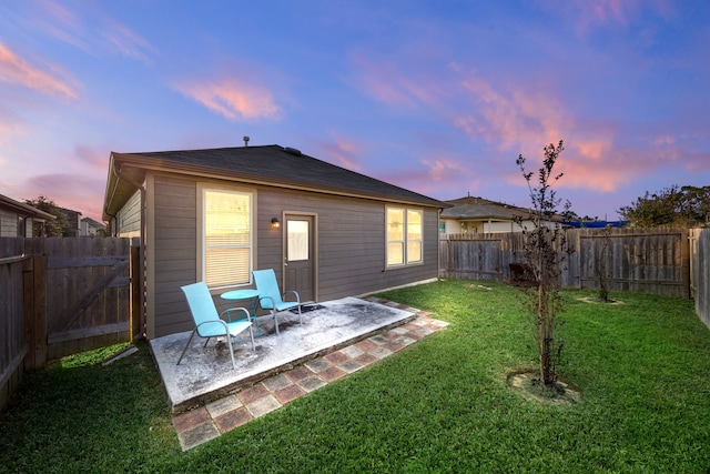 back house at dusk featuring a patio area and a lawn