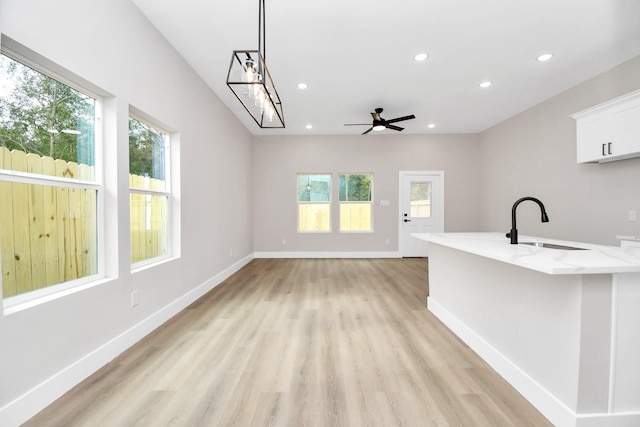 interior space with light stone countertops, white cabinets, sink, hanging light fixtures, and ceiling fan