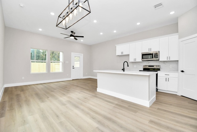 kitchen with ceiling fan, decorative light fixtures, an island with sink, stainless steel appliances, and white cabinets