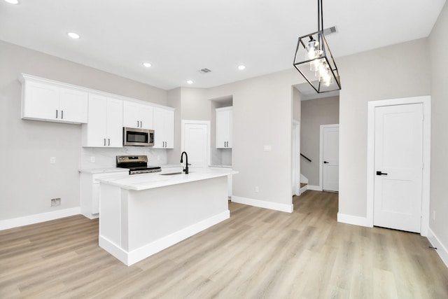 kitchen with stainless steel appliances, sink, white cabinetry, and an island with sink